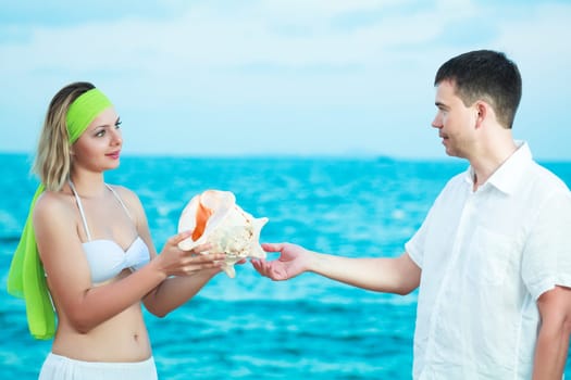 Young couple on the beach holding seashell
