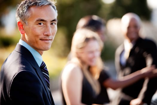 A group of business people outside - sharp focus on Asian man in foreground