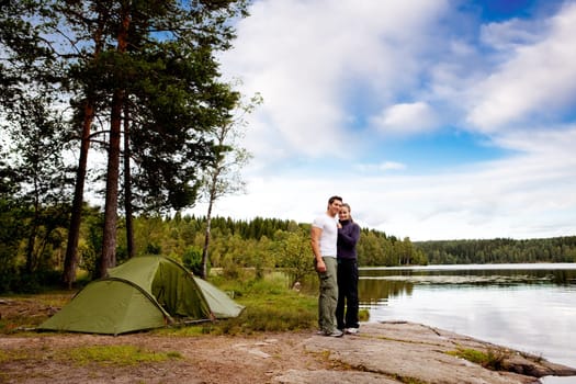 A couple of happy campers by a lake and forest