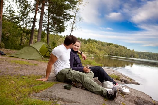 A man and woman happy camping in the forest by a lake