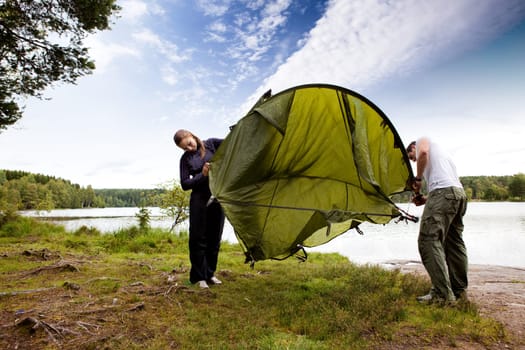 A couple setting up a tent in the forest by a lake