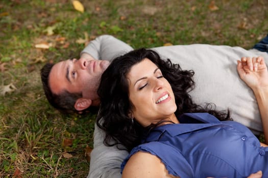 A couple laying on grass in a park daydreaming.  Focus on the womans eyes