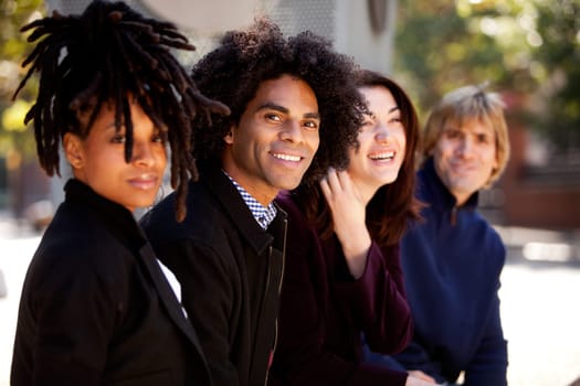 Group of four people of different ethnicities sitting in a row. Horizontally framed shot.
