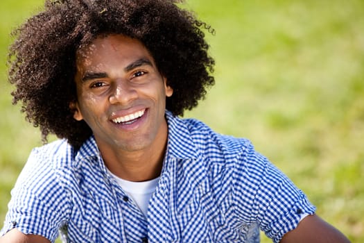 Young man smiling at camera in a park. Horizontally framed shot.