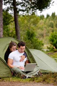 A man and woman using a computer outdoors in a tent