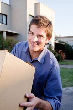 A happy man with a moving box in front of a house
