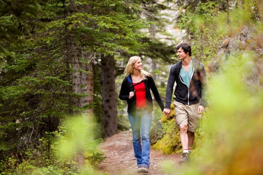 A happy couple looking at eachother and walking in the forest holding hands