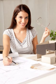 A young female architect at a desk with blueprints and model house