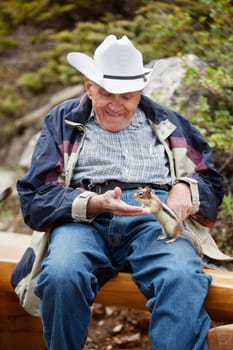 Happy relaxed senior man playing with squirrel - focus on squirrel