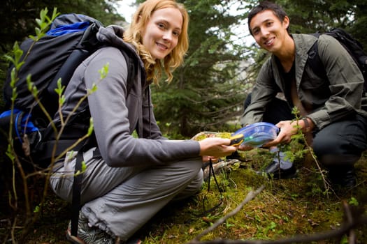 Two people finding a geocache in the forest.  Shallow depth of field with sharp focus on woman.