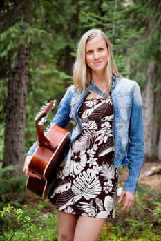 Attractive young female holding guitar against trees