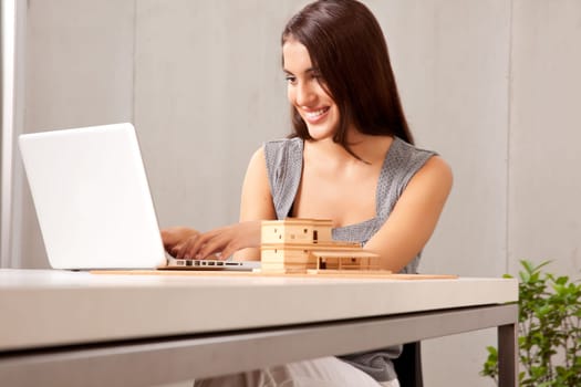 A creative professional woman working at a desk with a laptop and house model