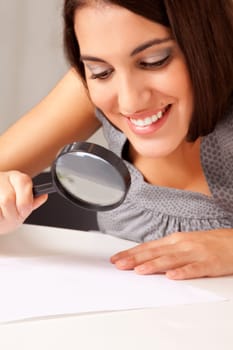 A prety brunette woman looking at a paper with a magnifying glass