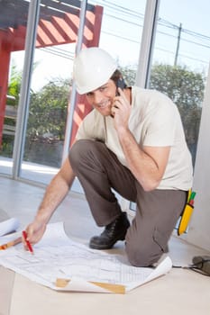 Portrait of a happy construction worker on cellphone with blueprint