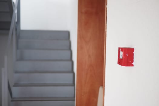 A red alarm system is mounted on the wall beside gray stairs.