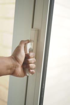 A hand is holding a door handle, poised to open a window.