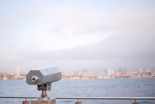 A viewfinder stands on a waterfront, offering a distant city view at dawn.