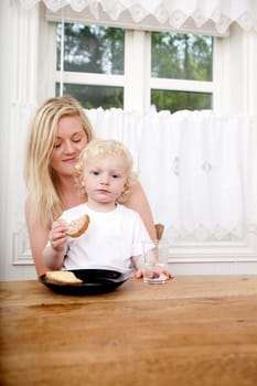 A young boy sitting on his mother's lap eating a sandwich
