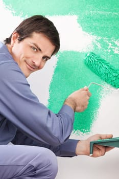 Portrait of smiling handsome man painting his house with roller