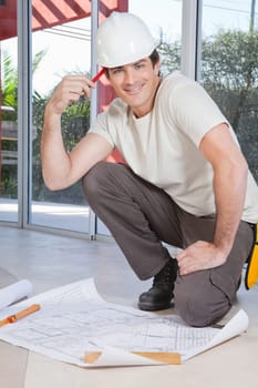 Smart young construction worker smiling with blueprint on floor