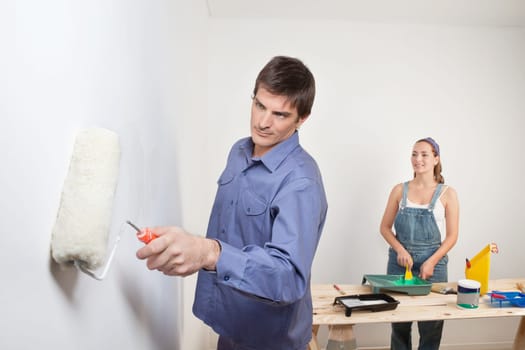 Serious man holding roller with woman in background