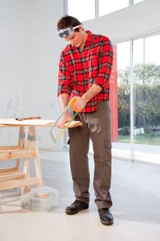 A carpenter cutting wood with a hand saw in a house