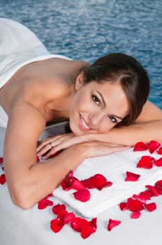 Beautiful young woman lying on massage bed with rose petals in foreground