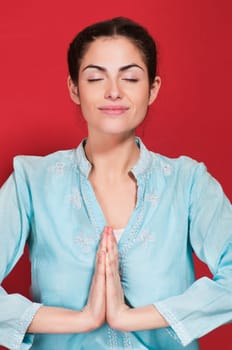 Smiling young woman with hands clasped against red background