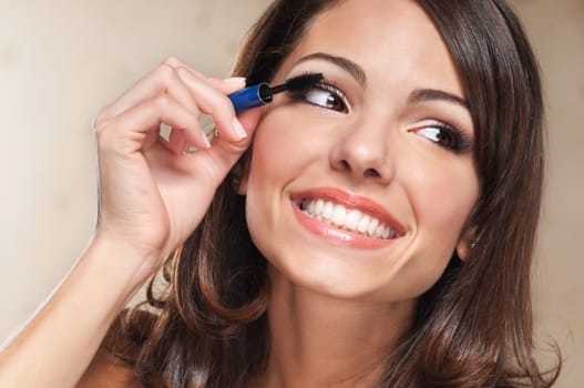 Beautiful smiling woman applying mascara on her eyelashes