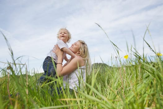 Low angle view of mother sitting on grass and playing with baby boy