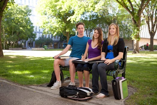 Group of students sitting on a bench on campus looking at the camera