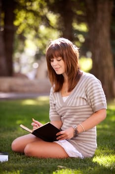 Pretty brunette student writing in a journal on a university campus