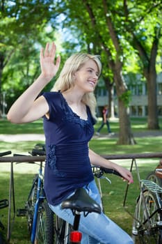 College student waving hand at someone while standing near by her bike