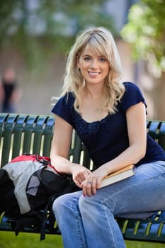 Portrait of young female student sitting on bench at college campus