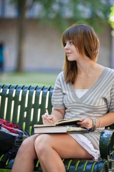 Young college girl sitting on bench with books and looking to side.