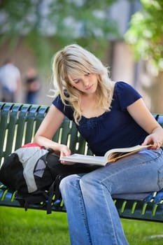 Young college student sitting on bench and reading book