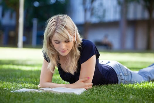 Pretty female reading book while lying on grass