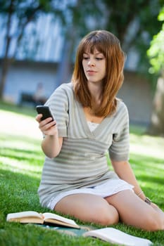 Young girl using cell phone while doing assignment on campus lawn