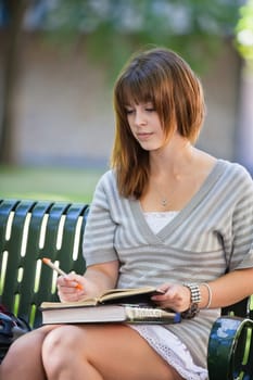 Young college student sitting on campus bench writing