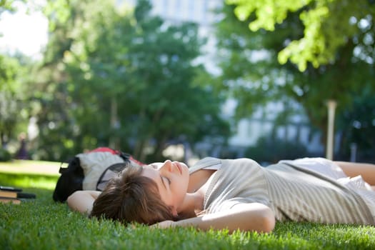 Young college student lying down on grass at campus lawn