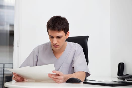 Serious male doctor reading reports of patient