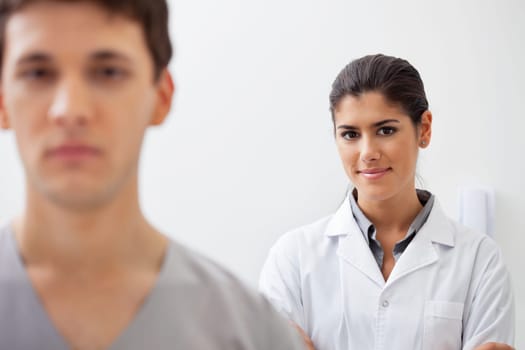 Portrait of smiling confident female doctor with colleague standing in front of her