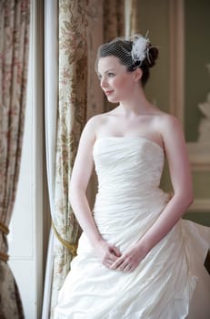 Pretty bride looking out of window and smiling on her wedding day