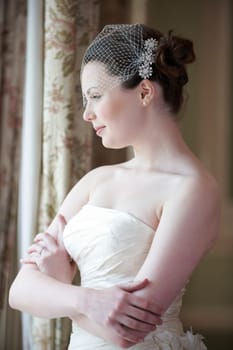 Pretty bride looking out of window and smiling on her wedding day