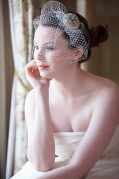 Pretty bride looking out of window and smiling on her wedding day