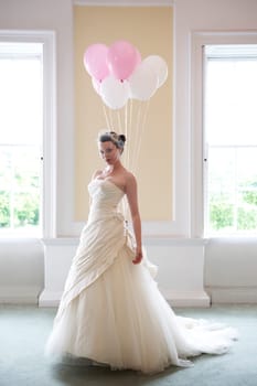 pretty bride in her wedding dress holding ballons in front of windows