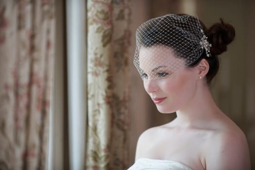 Pretty bride looking out of window and smiling on her wedding day