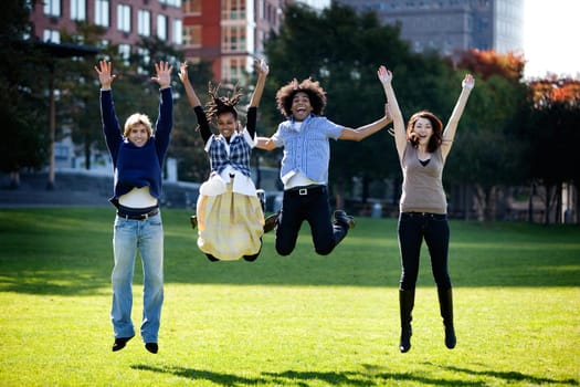 A group of happy people running towads the camera.  Sharp focus on rear three people, motion blur on front person.