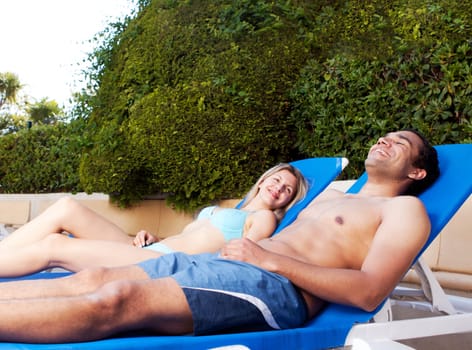 A couple suntanning on beach chairs beside a pool