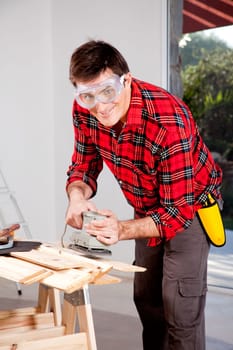 A man wearing saftey goggles using an electric hand sander